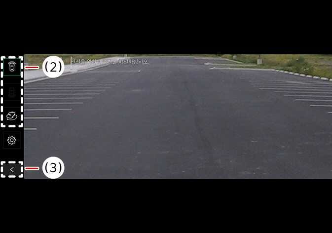 2026 Kia Tasman Surround View Monitor front view screen image. The screen displays the front camera view of a parking lot. On the left sidebar, callout (2) indicates the view switching button, and callout (3) indicates the back button with a left arrow icon. Explains the functions for switching camera views and returning to the previous screen.