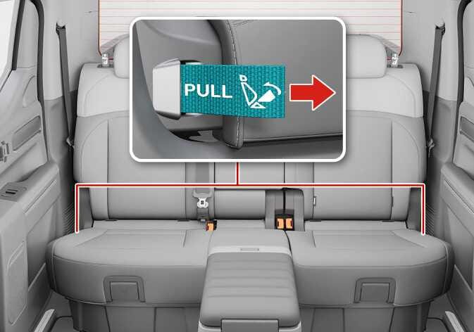2026 Kia Tasman rear seat storage operation image. A red outline highlights the space under the rear seats. A close-up shows a teal-highlighted strap labeled 'PULL' with a seat tip-up icon and a red arrow pointing to the right. Explains the function of pulling the strap to lift the seat cushion and access the storage space.