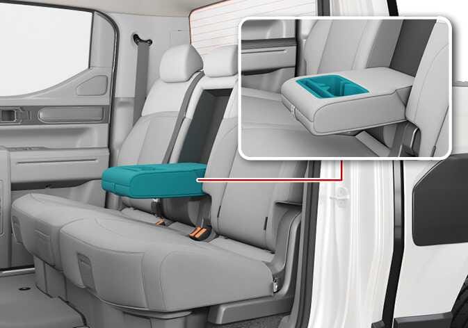 2026 Kia Tasman rear seat armrest image. The center armrest is highlighted in teal between the rear seats, and a magnified view connected by a red line displays the cup holders. Explains the function of utilizing the rear seat armrest.