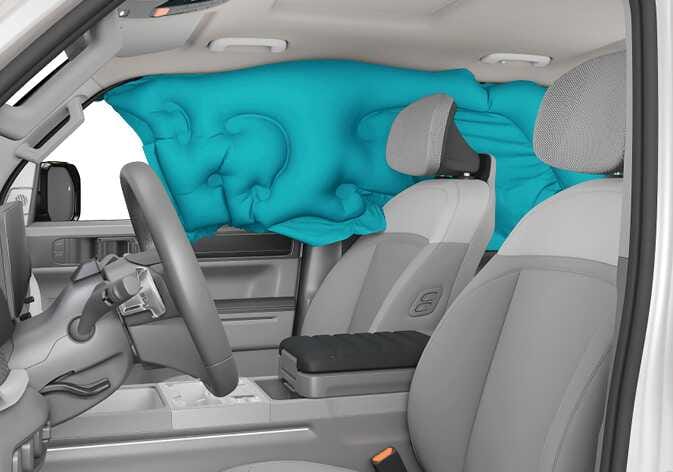 2026 Kia Tasman curtain airbag image. The interior view shows a curtain airbag highlighted in teal, deployed along the roof rail and covering the front and rear side windows. This illustrates the function of the airbag deploying to protect the heads of occupants during side impact collisions.