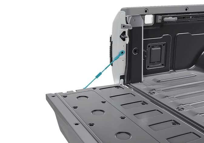 2026 Kia Tasman tailgate support strut image. The support cable connecting the open tailgate to the vehicle body is highlighted in teal. This illustrates the location of the strut to explain the precaution against holding or applying force to it.