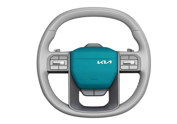 2026 Kia Tasman horn operation image. The center pad of the steering wheel is highlighted in teal. Explains the function of sounding the horn by pressing the center area.