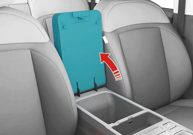 2026 Kia Tasman center console storage image. The center console lid is highlighted in teal, with a red curved arrow pointing upward to show the opening direction. Explains the function of opening the center console storage.