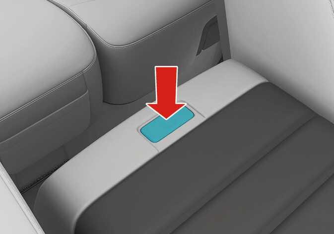 2026 Kia Tasman folding console table image. A red arrow points downward to the button highlighted in cyan on the back of the front seat armrest. Explains the function of pressing the button to use the folding console table.