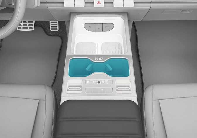 2026 Kia Tasman front seat cup holders image. The center console features two cup holders and a wireless charging tray highlighted in cyan. Explains the location and arrangement of the cup holders for the front seat.