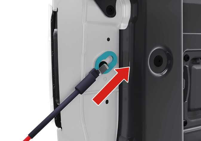 2026 Kia Tasman tailgate support cable detachment image. The keyhole-shaped slot on the white vehicle frame is highlighted in teal. A red arrow points upward, indicating the direction to push the black cable to release it from the bolt. Explains the process of detaching the cable from the bolt.