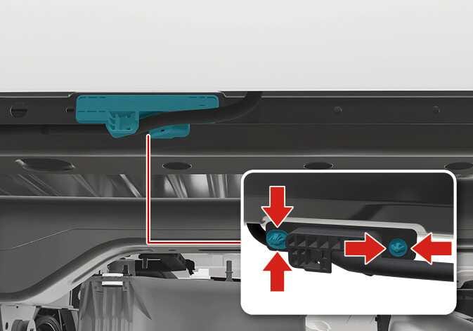 2026 Kia Tasman tailgate cable protector removal image. The cable protector is highlighted in cyan. A close-up shows red arrows pointing to the clips on the protector. Explains how to remove the clips and protector securing the cable.