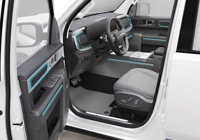 2026 Kia Tasman ambient light location image. The interior view with the driver's door open shows the ambient lighting areas highlighted in cyan on the instrument panel, door panels, and center console. Describes the installation locations of the interior mood lighting.