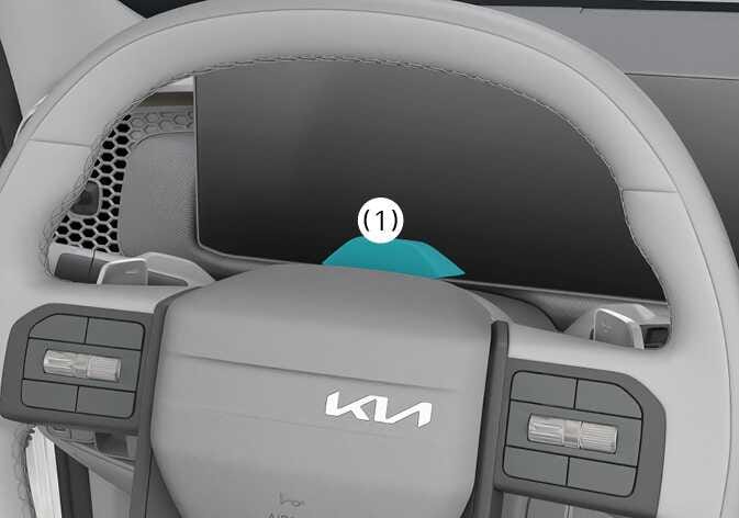 2026 Kia Tasman Forward Attention Warning detecting sensor image. The In-cabin camera (1) located on the steering column cover behind the steering wheel is highlighted in teal. Explains the location of the sensor that helps prevent driver distraction.