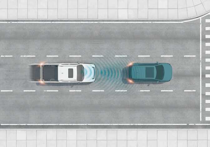 2026 Kia Tasman Forward Collision-Avoidance Assist basic function image. A top-down view shows a white pickup truck emitting blue sensor waves from the front towards a vehicle ahead. Explains the function of detecting a vehicle to warn the driver or assist with braking to avoid a collision.