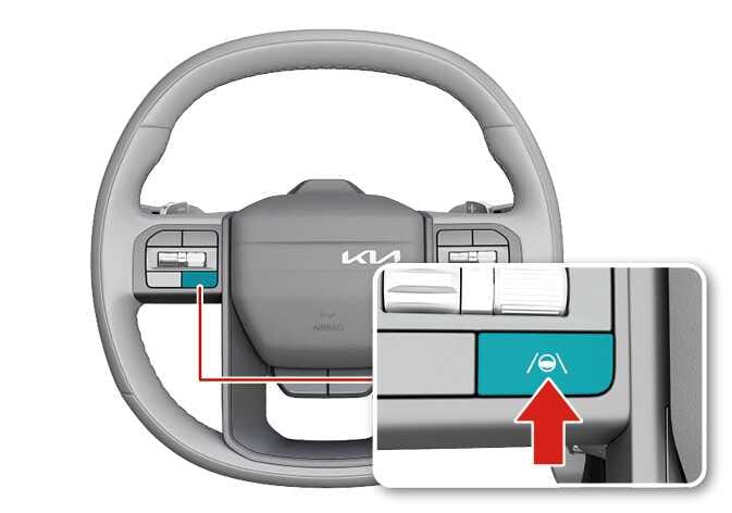 2026 Kia Tasman Lane Driving Assist button image. The button on the left spoke of the steering wheel is highlighted in teal. A close-up view shows the button with a car between lanes icon, and a red arrow points to it to indicate the pressing action. Explains the function of turning the Lane Keeping Assist system on or off.