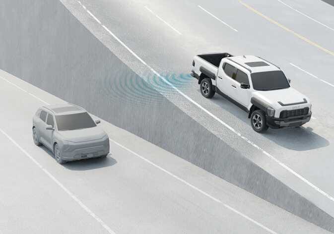2026 Kia Tasman Blind-Spot Collision-Avoidance Assist limitation image. A white pickup truck drives alongside a concrete wall, with a grey vehicle in the adjacent lane. Blue radar waves from the rear bumper are blocked by the wall. This explains the limitation where the detecting sensor is blocked by a wall or fixed object.