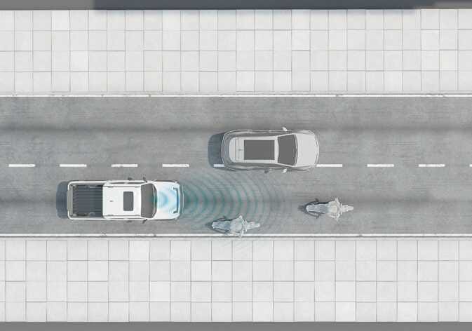 2026 Kia Tasman Smart Cruise Control limitation image. A top-down view shows the white vehicle in the lane emitting blue radar waves from the front. A grey SUV is in the adjacent lane, and two motorcycles are in the far lane. This illustrates the sensor's detection range and potential limitations in complex traffic situations.