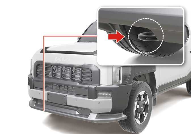 2026 Kia Tasman integrated front recovery hook image. A red line points from the lower front bumper to a close-up view where a red arrow indicates the recovery hook inside a white dotted circle. Explains the location of the integrated front recovery hook.