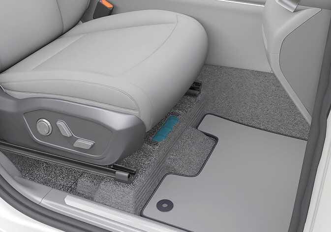 2026 Kia Tasman Vehicle Identification Number (VIN) location image. The image displays the floor area beneath the front passenger seat. A rectangular section on the floor frame is highlighted in teal, indicating the VIN stamp location. This explains where to find the VIN inside the vehicle.