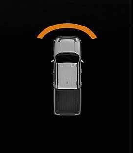 2026 Kia Tasman Forward Parking Distance Warning image. A top-down view of the silver vehicle shows an orange arc-shaped warning zone in front of the bumper on a black background. This illustrates the infotainment system alert for obstacles detected in the forward direction.