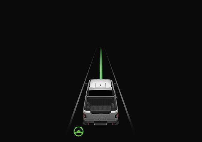 2026 Kia Tasman instrument cluster display image. A white vehicle travels between two white lane lines with a green path line ahead, accompanied by a green steering wheel icon at the bottom left. Explains the active Lane Following Assist function where lane markings are detected and steering is assisted.