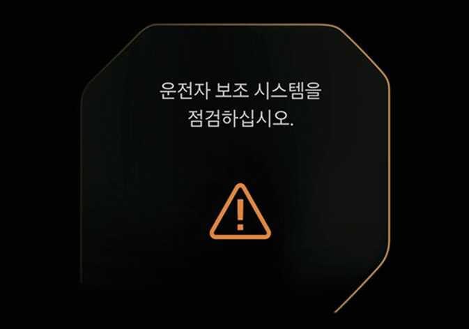 2026 기아 타스만 하이빔 보조 시스템 점검 경고문 이미지입니다. 클러스터 화면 중앙에 '운전자 보조 시스템을 점검하십시오.'라는 문구와 하단에 주황색 삼각형 느낌표 아이콘이 표시되어 있습니다. 시스템 이상 시 운전자에게 점검을 안내하는 화면 구성을 설명합니다.