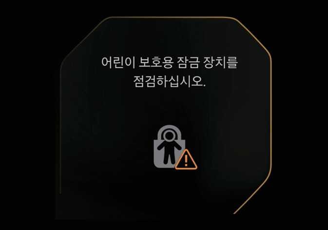 2026 기아 타스만 전자식 차일드 락 점검 경고 메시지 이미지입니다. 화면에 '어린이 보호용 잠금 장치를 점검하십시오.' 문구와 자물쇠 속 어린이 형상, 주황색 느낌표 아이콘이 표시되어 있습니다. 시스템 이상 시 점검이 필요함을 알리는 화면을 설명합니다.