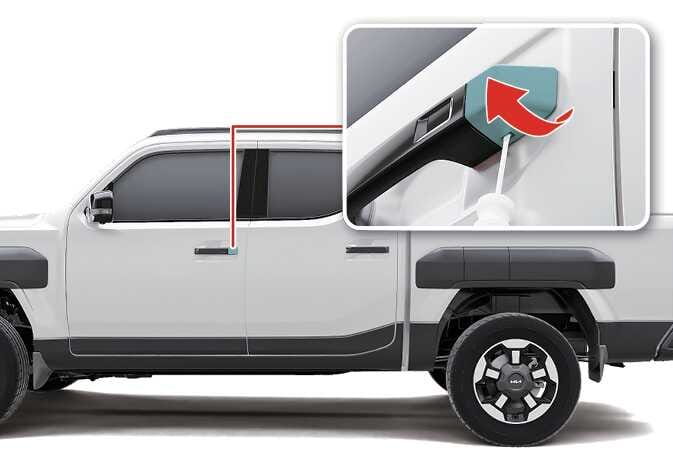 2026 기아 타스만 비상 키 사용을 위한 도어 핸들 커버 분리 이미지입니다. 운전석 도어 핸들 위치와 확대된 상세도가 표시되어 있습니다. 상세도에서는 청록색으로 강조된 커버 하단 홈에 도구를 삽입한 후, 붉은색 화살표가 가리키는 방향으로 커버를 들어 올려 분리하는 동작을 보여줍니다. 비상시 물리 키를 사용하기 위해 커버를 탈거하는 기능을 설명합니다.