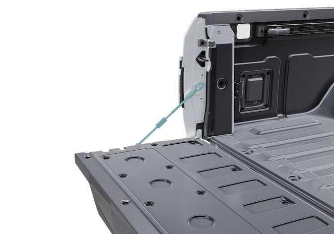 2026 기아 타스만 테일게이트 지지 케이블 이미지입니다. 테일게이트가 열린 상태에서 차체와 테일게이트를 연결하는 지지 케이블이 청록색으로 강조되어 있습니다. 안전사고 예방을 위해 잡거나 힘을 가하지 말아야 할 부품의 위치를 설명합니다.