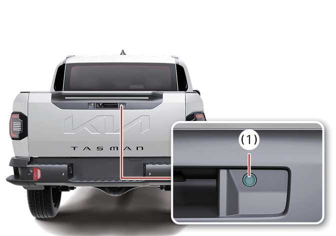 2026 기아 타스만 디지털 센터 미러 카메라 장착 위치 이미지입니다. 차량 후면 테일게이트 핸들 부근에서 붉은색 선으로 연결된 상세도에 청록색으로 강조된 카메라(1)가 표시되어 있습니다. 디지털 센터 미러에 후방 영상을 송출하는 카메라의 정확한 위치를 설명합니다.