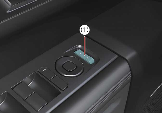 2026 기아 타스만 실외 미러 조절 선택 스위치 이미지입니다. L과 R 문구가 있는 스위치가 청록색으로 강조되어 (1)번으로 표시되어 있습니다. 스위치 위치를 조작하여 후진 시 실외 미러 자동 조절 기능을 설정하는 방법을 설명합니다.