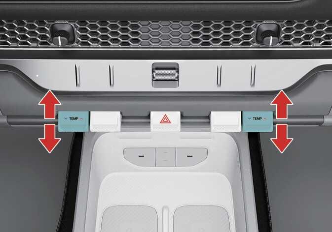 2026 기아 타스만 온도 조절 레버 이미지입니다. 청록색으로 강조된 TEMP 문구가 표시된 레버 양옆에 위아래 방향을 지시하는 굵은 붉은색 화살표가 표시되어 있습니다. 레버를 위로 올리거나 아래로 내려 실내 온도를 조절하는 기능을 설명합니다.