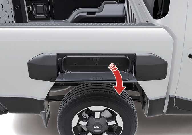 2026 기아 타스만 사이드 스토리지 이미지입니다. 적재함 측면 휠 하우스 상단의 수납함 도어가 열려 있습니다. 붉은색 굽은 화살표가 도어가 아래로 열리는 방향을 지시합니다. 도어를 열어 수납 공간을 사용하거나 테이블로 활용하는 기능을 설명합니다.
