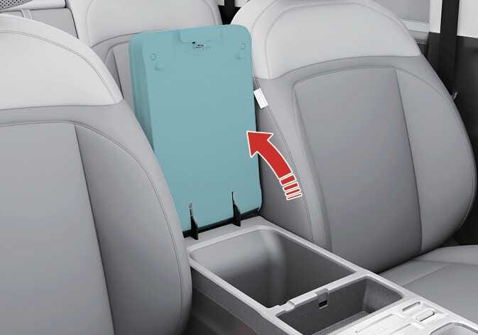 2026 기아 타스만 중앙 콘솔 박스 이미지입니다. 운전석과 동승석 사이에 위치한 콘솔 박스 덮개가 청록색으로 강조되어 있으며, 덮개가 열려 내부 수납공간이 보입니다. 굵은 붉은색 굽은 화살표가 덮개를 뒤쪽 위로 들어 올리는 개방 방향을 지시하고 있습니다. 레버를 당겨 보관함 커버를 열고 내부 수납공간을 사용하는 기능을 설명합니다.