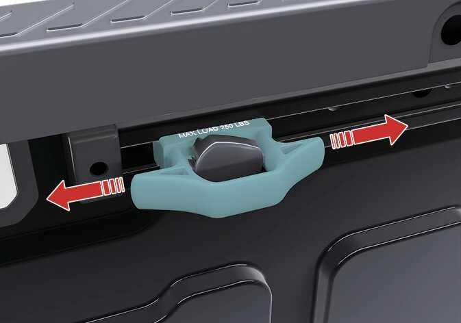 2026 기아 타스만 레일 및 클릿 조작 이미지입니다. 적재함 레일에 장착된 청록색으로 강조된 클릿과, 이를 좌우로 이동시키는 방향을 지시하는 빨간색 화살표가 표시되어 있습니다. 클릿 상단에는 'MAX LOAD 250 LBS' 문구가 적혀 있습니다. 레일을 따라 클릿을 좌우로 밀어 원하는 위치로 이동시키는 기능을 설명합니다.