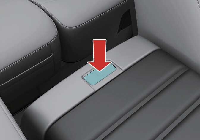 2026 기아 타스만 폴딩 콘솔 테이블 조작 버튼 이미지입니다. 앞좌석 암레스트 뒤쪽에 위치한 버튼이 청록색으로 강조되어 있으며, 굵은 빨간색 화살표가 아래 방향으로 버튼을 누르도록 지시하고 있습니다. 버튼을 눌러 폴딩 콘솔 테이블을 사용할 수 있도록 잠금을 해제하는 기능을 설명합니다.