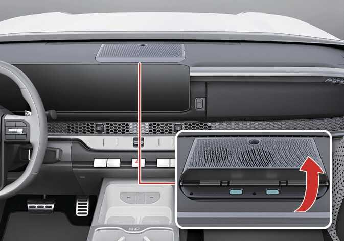 2026 기아 타스만 인스트루먼트 패널 충전용 USB 단자 이미지입니다. 동승석 대시보드 상단의 덮개를 위쪽으로 들어 올리는 동작을 굵은 빨간색 굽은 화살표로 지시하고 있습니다. 덮개 안쪽에는 청록색으로 강조된 두 개의 USB 단자가 위치해 있습니다. 덮개를 열어 충전용 USB 단자를 사용하는 기능을 설명합니다.