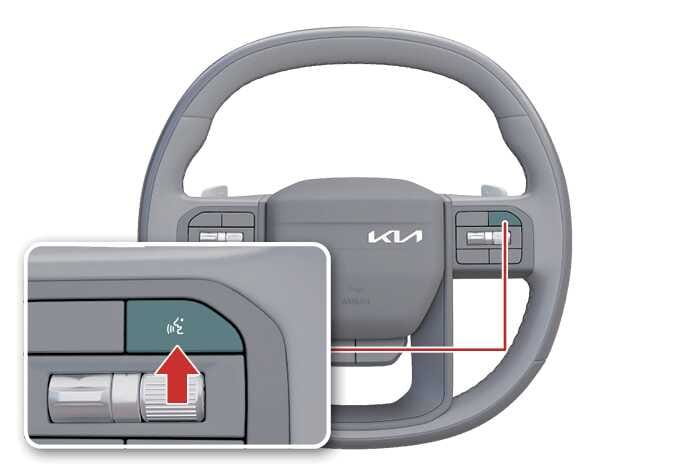 2026 기아 타스만 음성인식 시스템 조작 버튼 이미지입니다. 스티어링 휠 우측 리모컨 키 중 얼굴 모양의 아이콘이 그려진 음성인식 버튼이 청록색으로 강조되어 있으며, 상세도에는 붉은색 화살표가 해당 버튼을 가리키고 있습니다. 인포테인먼트 시스템 제어를 위해 음성인식 기능을 실행하는 버튼의 위치를 설명합니다.