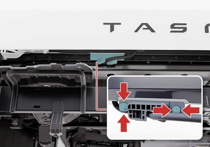 2026 기아 타스만 테일게이트 하단 케이블 분리 이미지입니다. 뒷범퍼 하단에 위치한 케이블 연결 부위가 청록색으로 강조되어 있습니다. 확대된 상세도에는 고정 장치의 양쪽을 안쪽으로 누르고 위로 밀어 올리는 동작을 지시하는 붉은색 화살표가 표시되어 있습니다. 뒷범퍼 하단의 케이블을 분리하는 기능을 설명합니다.