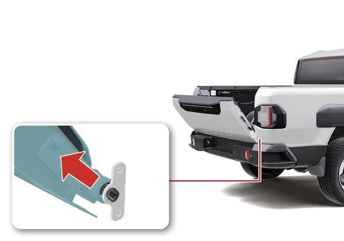 2026 기아 타스만 테일게이트 하단 케이블 분리 이미지입니다. 테일게이트가 열린 상태에서 하단 연결 부위를 확대한 상세도가 있습니다. 청록색으로 강조된 케이블 부품을 붉은색 화살표 방향인 대각선 위로 당겨, 뒷범퍼 하단에 위치한 케이블을 분리하는 과정을 설명합니다.