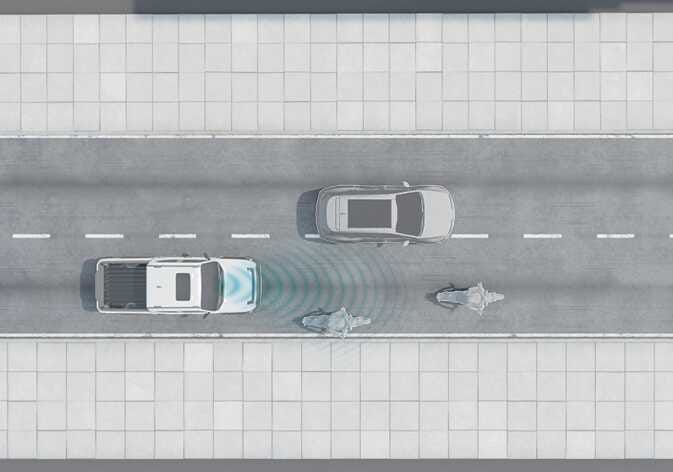 2026 기아 타스만 스마트 크루즈 컨트롤 작동 제한 사항 이미지입니다. 주행 중인 흰색 차량의 전방 센서가 청록색 파장으로 인접 차선의 승용차와 오토바이를 탐지하는 모습을 보여줍니다. 오토바이와 같이 폭이 좁은 차량을 인식할 때 발생할 수 있는 시스템의 작동 제한 상황을 설명합니다.