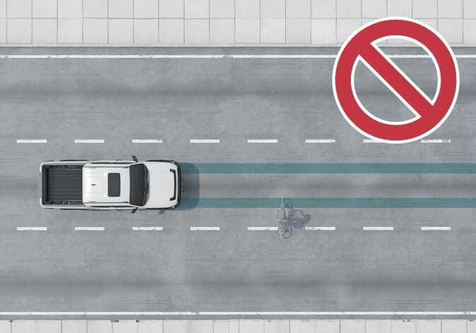 2026 기아 타스만 회피 조향 보조 제한 사항 이미지입니다. 청록색으로 강조된 차로 위를 자전거 탑승자가 가로지르는 모습과 우측 상단에 붉은색 금지 기호가 표시되어 있습니다. 보행자 및 자전거 탑승자가 차량의 주행 방향과 교차로 움직일 경우 기능이 정상적으로 작동하지 않을 수 있음을 설명합니다.