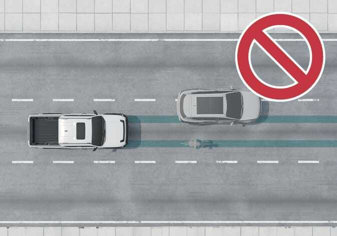 2026 기아 타스만 회피 조향 보조 제한 사항 이미지입니다. 흰색 트럭 전방에 자전거 탑승자가 있고, 옆 차로에 회색 차량이 있어 회피할 공간이 없는 상황을 보여줍니다. 우측 상단에는 붉은색 금지 기호가 표시되어 있습니다. 작동 범위 내에 있는 보행자 및 자전거 탑승자를 피할 수 있는 공간이 충분하지 않을 때 기능이 제한됨을 설명합니다.