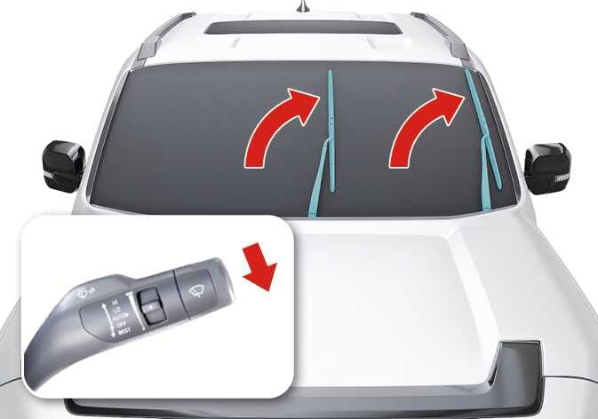 2026 기아 타스만 와이퍼 블레이드 교체 방법 이미지입니다. 청록색으로 강조된 와이퍼가 붉은색 굽은 화살표를 따라 위로 올라가는 모습과, 와이퍼 레버를 MIST 위치인 아래로 내리는 붉은색 화살표가 상세도로 표시되어 있습니다. 와이퍼를 교체 위치로 이동시키는 기능을 설명합니다.