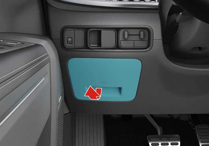 2026 기아 타스만 실내 퓨즈 박스 커버 분리 이미지입니다. 운전석 스티어링 휠 좌측 대시보드 하단에 위치한 퓨즈 박스 커버가 청록색으로 강조되어 있습니다. 커버 손잡이 부분에 굵은 빨간색 화살표가 몸 쪽으로 당기는 방향을 나타내고 있습니다. 손잡이를 잡아당겨 퓨즈 박스 커버를 분리하는 기능을 설명합니다.