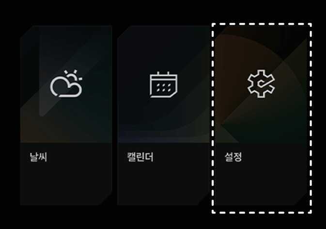 2026 기아 타스만 인포테인먼트 시스템 홈 화면 이미지입니다. 날씨, 캘린더, 설정 메뉴 중 우측의 톱니바퀴 아이콘과 '설정' 텍스트가 표시된 메뉴가 점선 박스로 강조되어 있습니다. 시스템 화면에서 설정 메뉴를 선택하여 차량 설정 화면으로 이동하는 단계를 설명합니다.