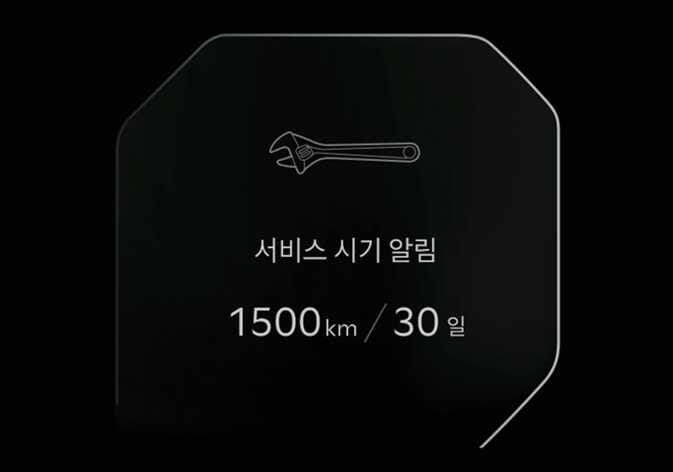 2026 기아 타스만 서비스 알림 모드 화면 이미지입니다. 검은색 배경의 LCD 화면 상단에 스패너 아이콘이 있고, 중앙에 '서비스 시기 알림' 문구가 표시되어 있습니다. 하단에는 잔여 주행 거리 '1500 km'와 잔여 기간 '30 일'이 흰색 텍스트로 나타나 있습니다. 정기 점검까지 남은 거리와 시간을 운전자에게 안내하는 기능을 설명합니다.