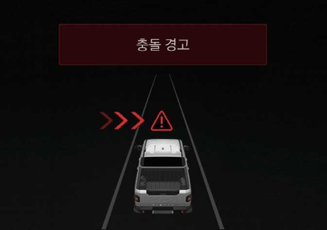 2026 기아 타스만 전방 교차 충돌 경고 이미지입니다. 검은색 배경 화면 상단에 붉은색 박스와 '충돌 경고' 문구가 표시되어 있습니다. 흰색 차량 전방 좌측에 붉은색 화살표와 삼각형 느낌표 아이콘이 나타나 교차로에서 접근하는 차량의 위험을 시각적으로 보여줍니다. 전방 교차 충돌 위험 시 운전자에게 경고하는 기능을 설명합니다.