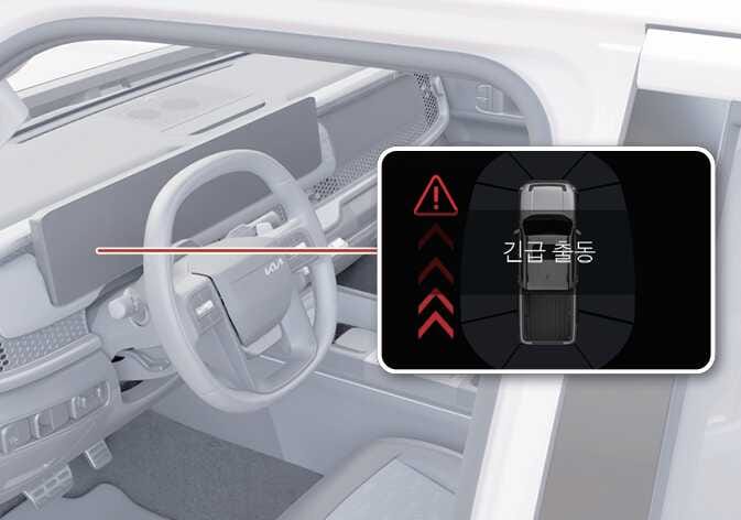 2026 기아 타스만 충돌방지 보조(출차) 경고 화면 이미지입니다. 운전석 대시보드와 스티어링 휠을 배경으로, 계기판에 나타나는 경고 상황을 붉은색 선으로 연결하여 확대한 상세 이미지가 포함되어 있습니다. 검은색 배경의 화면 중앙에는 차량 그래픽이 위치하고, 좌측에는 후방에서 접근하는 위험을 알리는 붉은색 화살표 아이콘과 삼각형 느낌표 경고등이 표시되어 있습니다. 차량 그래픽 위에는 '긴급 출동'이라는 경고 문구가 있습니다. 후측방에서 접근하는 차량과의 충돌 위험을 감지했을 때 운전자에게 경고하고 제동을 돕는 기능을 설명합니다.