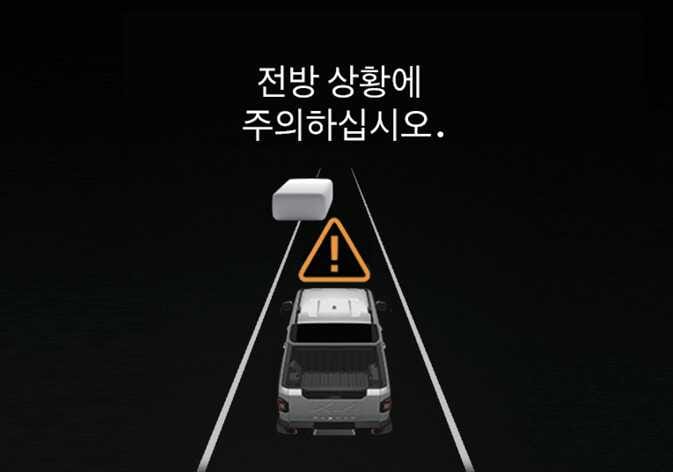 2026 기아 타스만 전방 상황 주의 알림 이미지입니다. 도로 위 주행 중인 차량과 전방의 물체 사이에 주황색 삼각형 느낌표 경고 아이콘이 떠 있고, 상단에 '전방 상황에 주의하십시오.'라는 문구가 표시되어 있습니다. 스마트 크루즈 컨트롤 작동 중 전방 차량이 사라졌을 때 경고를 통해 주의를 환기하는 기능을 설명합니다.