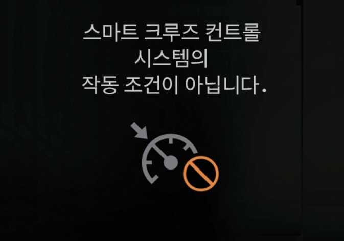 2026 기아 타스만 스마트 크루즈 컨트롤 비작동 알림 화면 이미지입니다. 화면 중앙에 '스마트 크루즈 컨트롤 시스템의 작동 조건이 아닙니다.'라는 문구가 표시되어 있습니다. 하단에는 회색 속도계 아이콘에 주황색 금지 표시가 겹쳐진 그래픽이 있습니다. 작동 조건이 충족되지 않았을 때 경고 문구와 아이콘으로 운전자에게 알리는 기능을 설명합니다.
