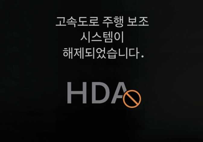 2026 기아 타스만 고속도로 주행 보조 해제 알림 화면 이미지입니다. '고속도로 주행 보조 시스템이 해제되었습니다.'라는 문구와 HDA 텍스트 옆에 주황색 금지 아이콘이 표시되어 있습니다. 스티어링 휠을 잡지 않아 시스템이 종료되는 상황을 설명합니다.