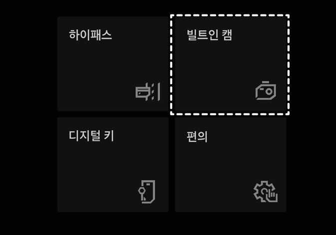 2026 기아 타스만 인포테인먼트 시스템 메뉴 화면 이미지입니다. 검은색 배경의 화면에 '하이패스', '디지털 키', '편의' 메뉴와 함께 카메라 아이콘이 포함된 '빌트인 캠' 메뉴가 표시되어 있습니다. 특히 '빌트인 캠' 메뉴가 흰색 점선 박스로 강조되어 있습니다. 저장된 영상을 확인하기 위해 시스템에서 해당 메뉴를 선택하는 기능을 설명합니다.