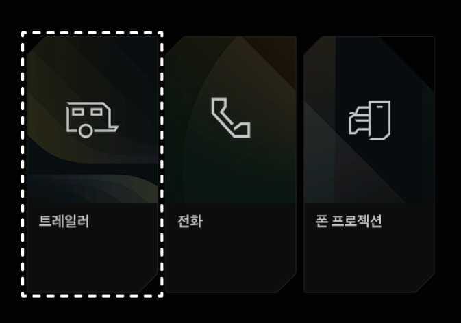 2026 기아 타스만 인포테인먼트 시스템 홈 화면의 트레일러 메뉴 이미지입니다. 화면에는 트레일러 아이콘과 '트레일러', 전화기 아이콘과 '전화', 차량 및 스마트폰 아이콘과 '폰 프로젝션' 메뉴 버튼이 나열되어 있습니다. 인포테인먼트 시스템의 홈 화면에서 트레일러 메뉴를 선택하여 트레일러 설정을 진행하는 기능을 설명합니다.